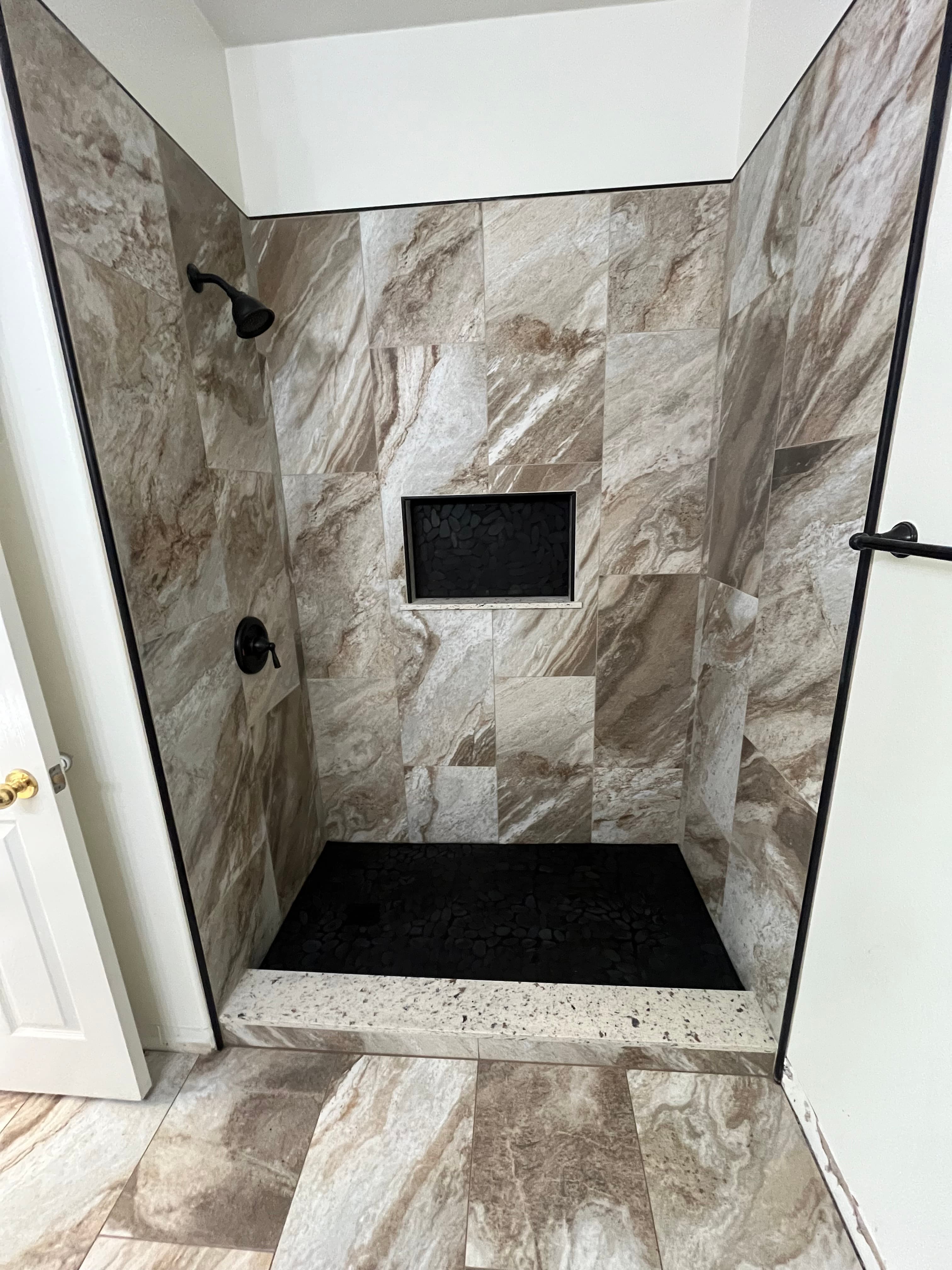 Walk-in shower with natural stone tile and black pebble niche accent in Murrieta