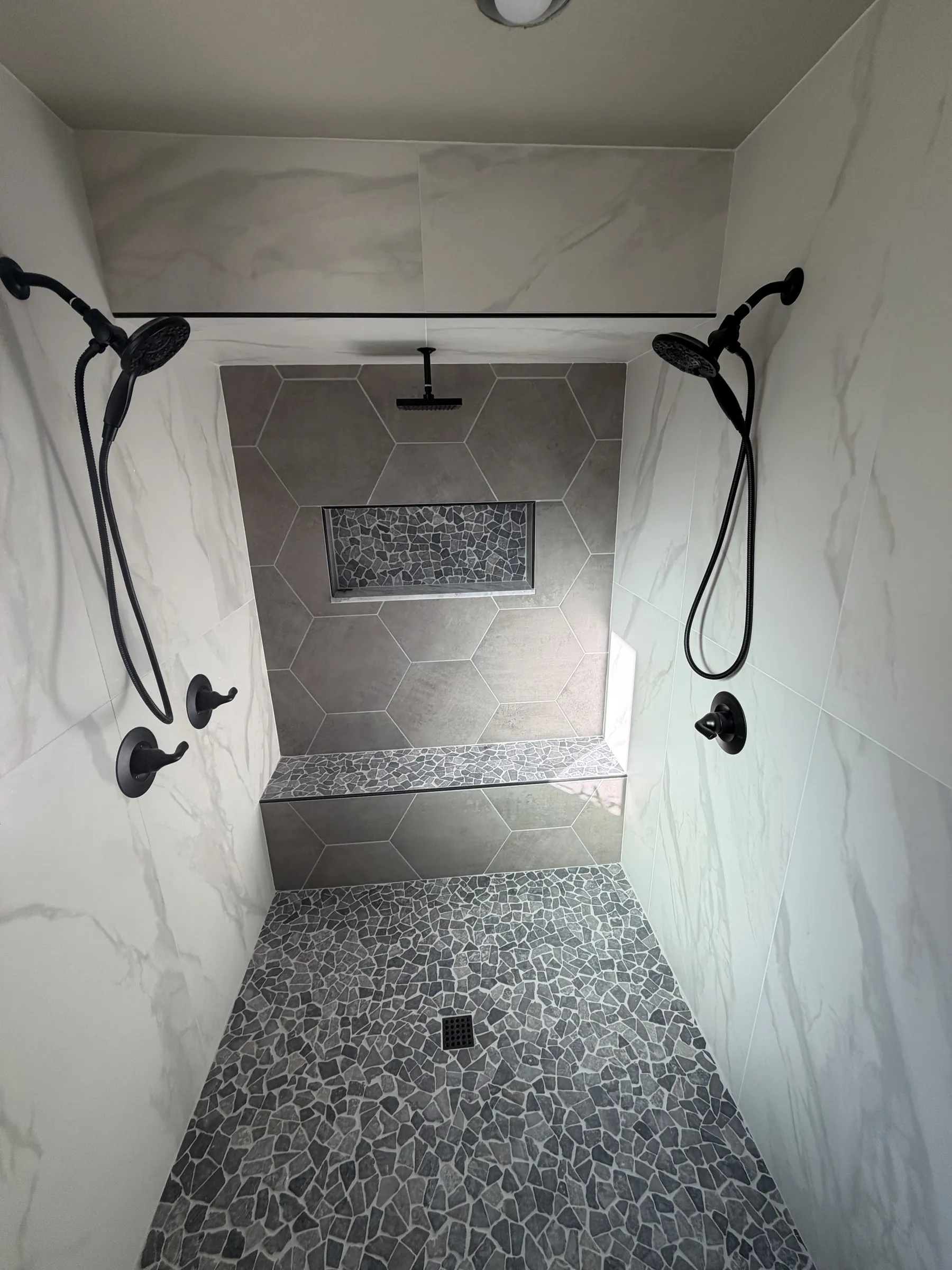 Curbless walk-in shower with hexagon tile accent wall and pebble floor installed by Cutting Edge Tile & Stone