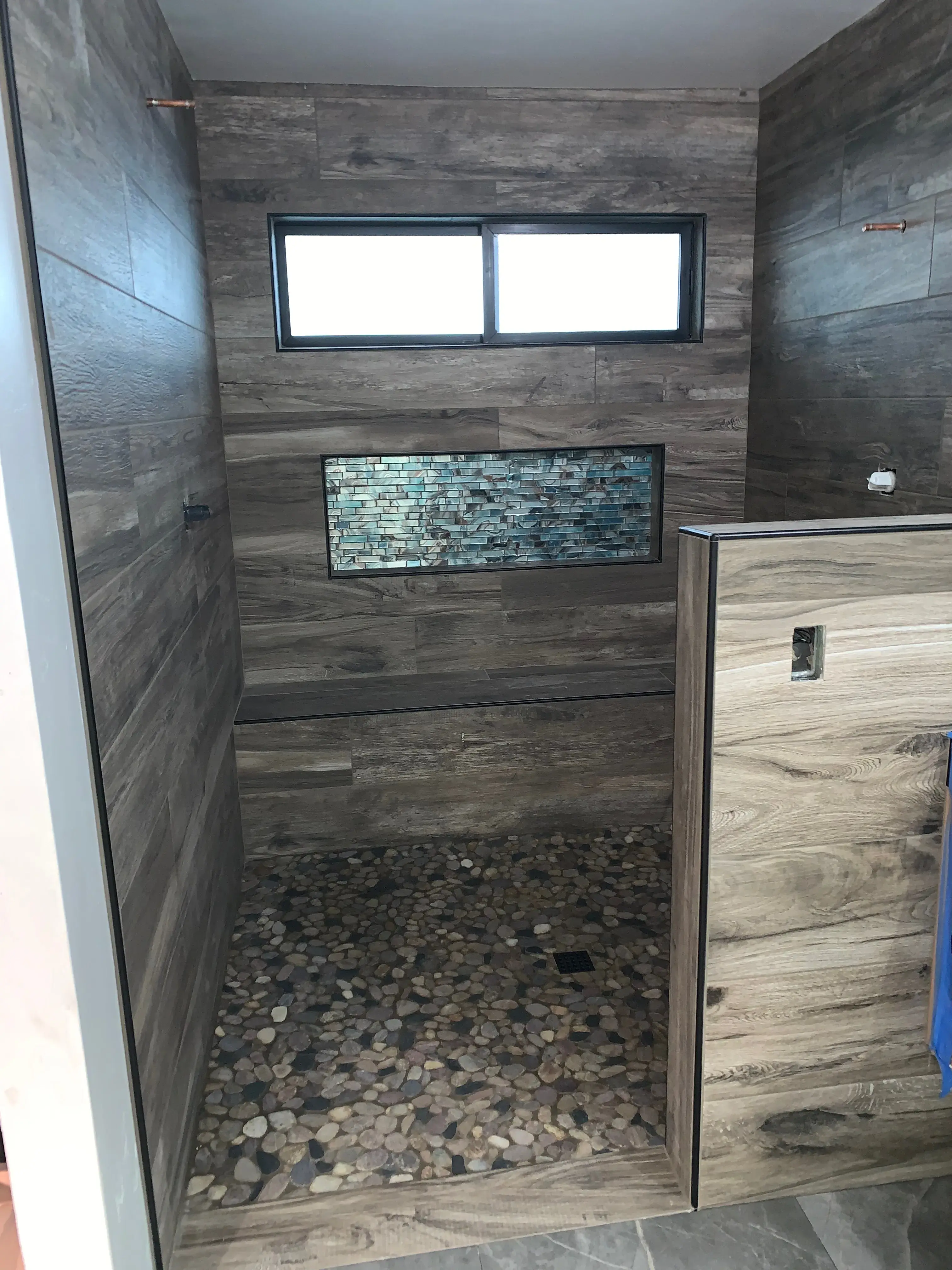 Walk-in shower with decorative glass mosaic accent panel and pebble stone floor in Fallbrook