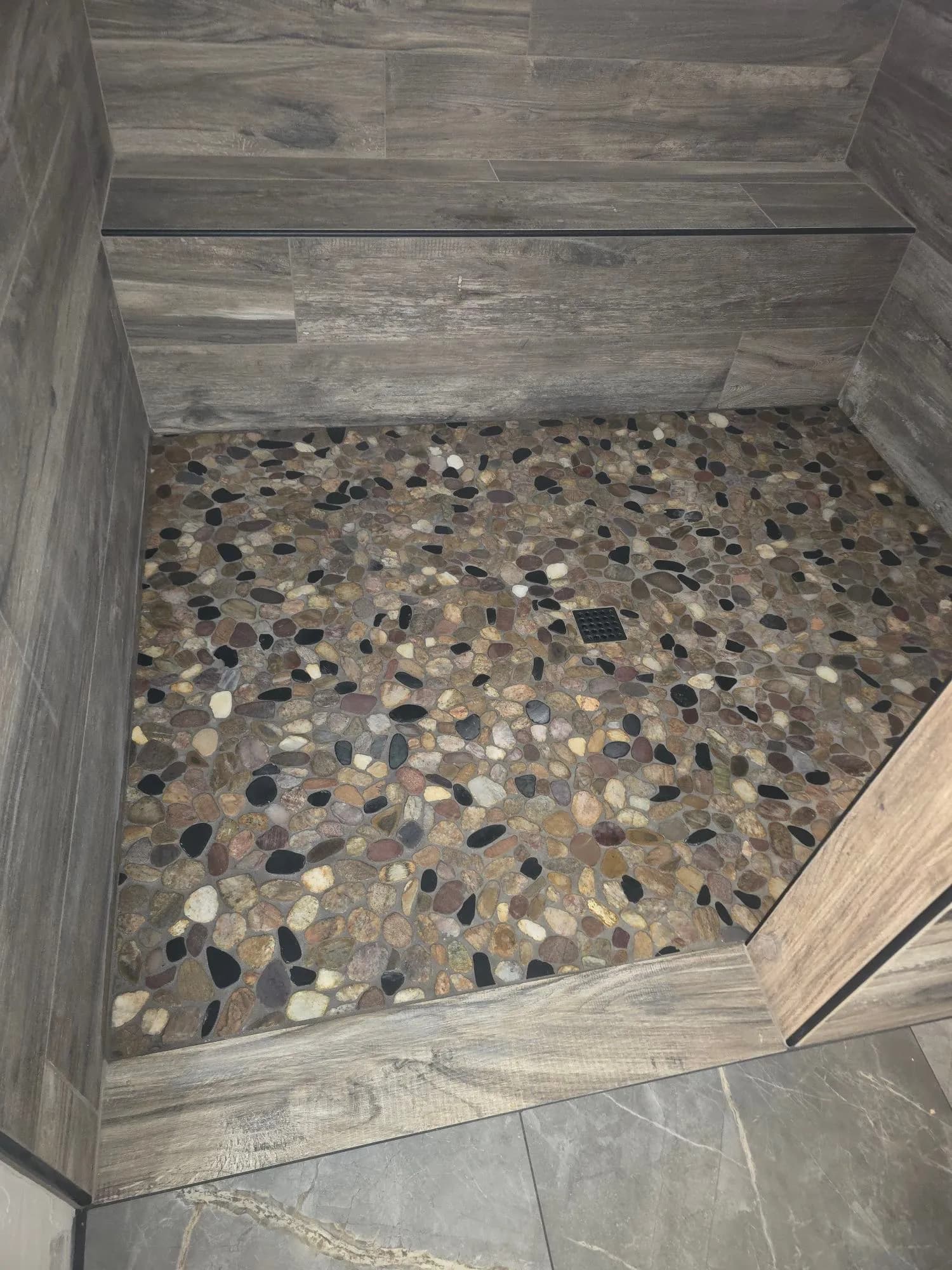 Custom pebble stone mosaic shower floor with wood-look plank tile surround in Fallbrook bathroom