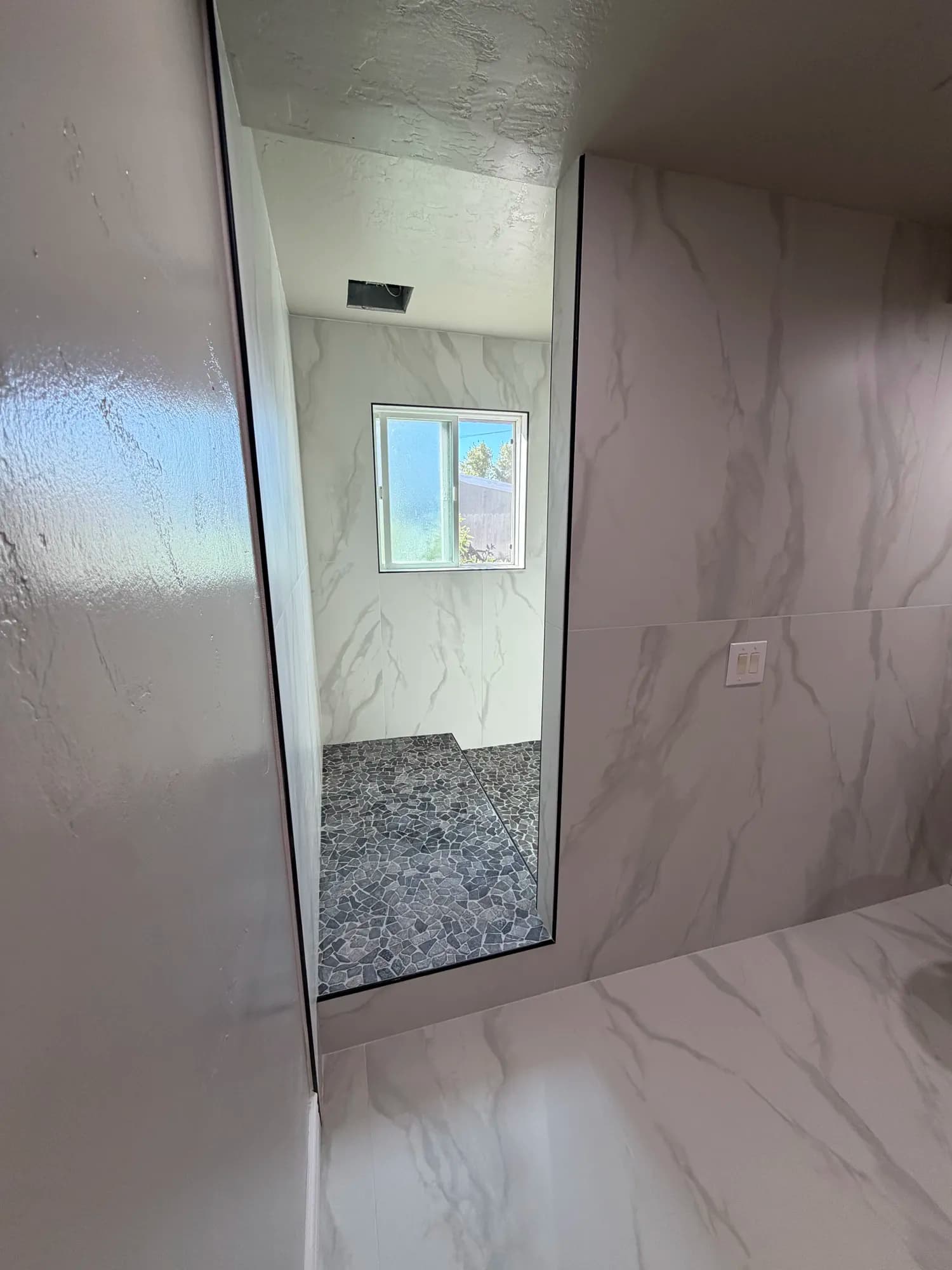 Curbless shower entry with marble-look porcelain walls and pebble stone floor in Menifee, Schluter waterproofed