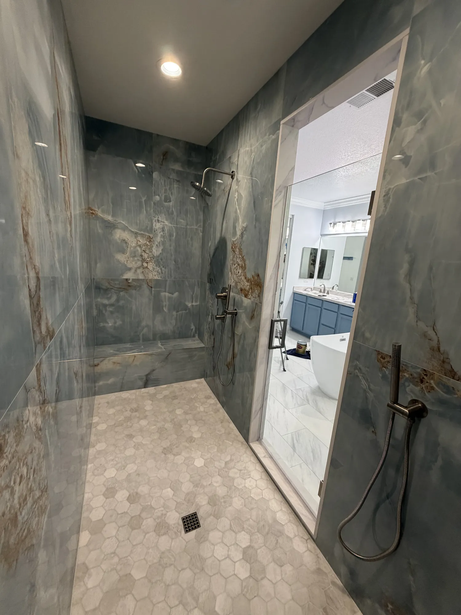 Walk-in shower with floor-to-ceiling blue onyx-look porcelain slabs, hexagon mosaic floor and frameless glass in Murrieta home